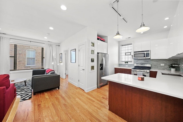 kitchen with light hardwood / wood-style floors, appliances with stainless steel finishes, backsplash, pendant lighting, and sink