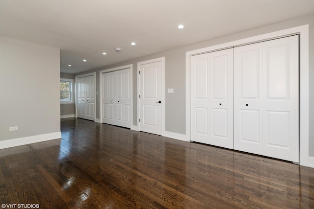 unfurnished bedroom with dark hardwood / wood-style flooring and two closets