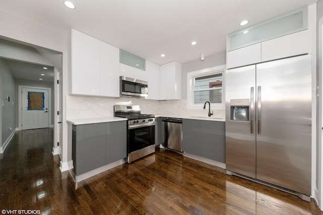 kitchen featuring dark wood-type flooring, sink, white cabinetry, stainless steel appliances, and decorative backsplash