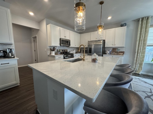 kitchen featuring white cabinetry, hanging light fixtures, a center island with sink, and appliances with stainless steel finishes