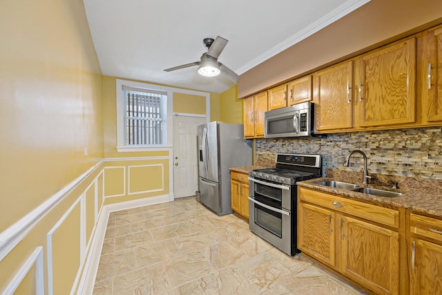 kitchen with stainless steel appliances, sink, ornamental molding, ceiling fan, and dark stone counters