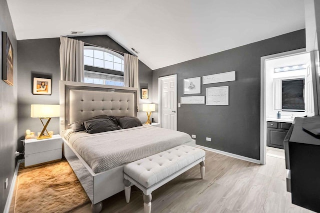 bedroom with vaulted ceiling, light hardwood / wood-style floors, and ensuite bath