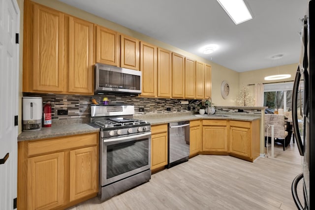 kitchen with appliances with stainless steel finishes, decorative backsplash, light brown cabinetry, kitchen peninsula, and light wood-type flooring