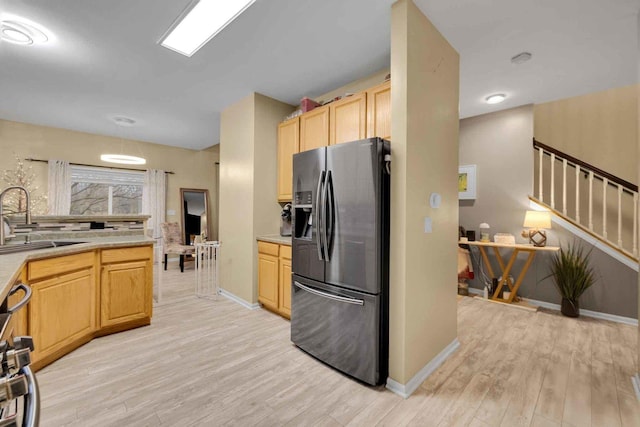 kitchen featuring stove, sink, light hardwood / wood-style flooring, light brown cabinetry, and stainless steel fridge