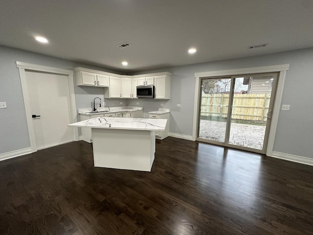 kitchen featuring visible vents, dark wood-type flooring, white cabinetry, stainless steel microwave, and a center island