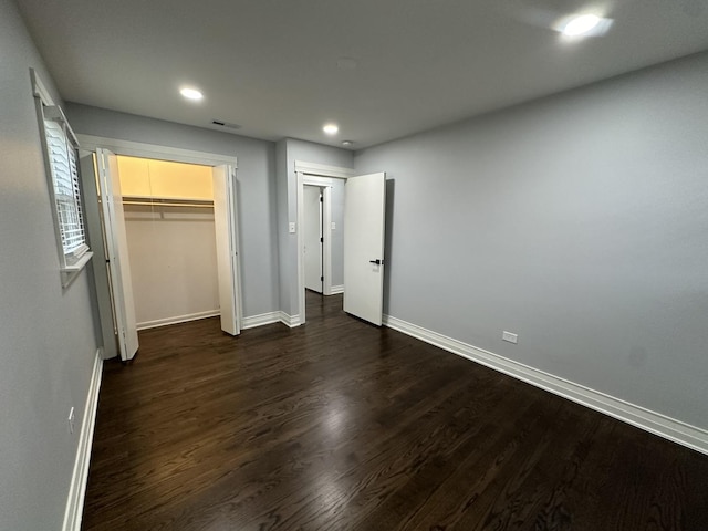 unfurnished bedroom featuring dark wood-type flooring, a walk in closet, and a closet