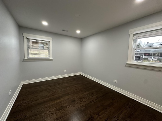 empty room with dark wood finished floors, recessed lighting, baseboards, and visible vents