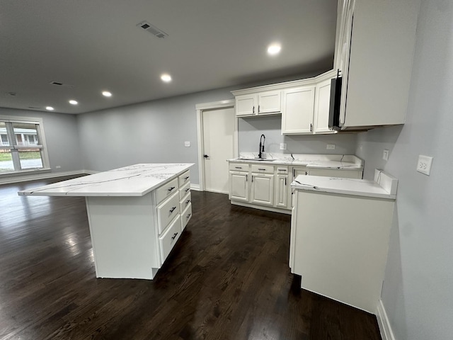 kitchen with visible vents, a sink, dark wood finished floors, a center island, and white cabinets