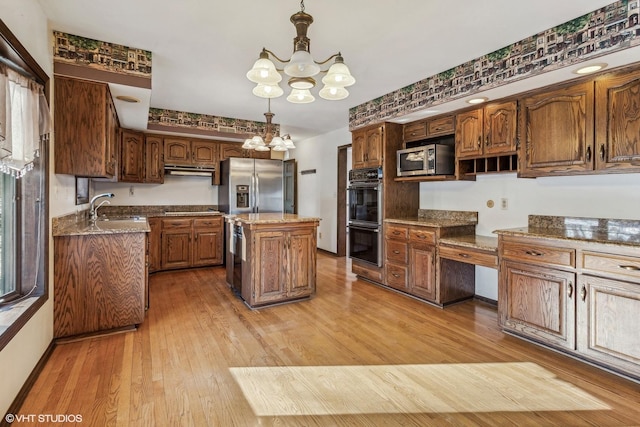 kitchen featuring black appliances, pendant lighting, a kitchen island, sink, and an inviting chandelier