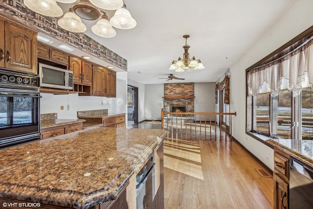 kitchen featuring pendant lighting, light hardwood / wood-style floors, a brick fireplace, stone counters, and appliances with stainless steel finishes