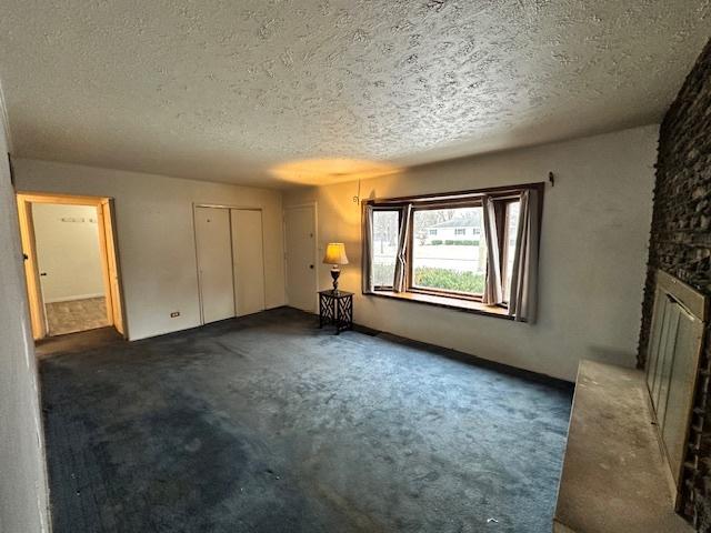 interior space with a textured ceiling, dark carpet, and a stone fireplace