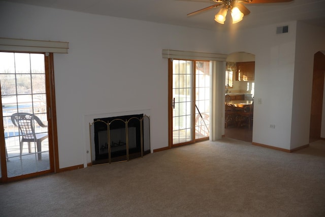 unfurnished living room with visible vents, arched walkways, baseboards, carpet floors, and a fireplace