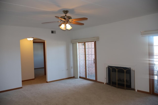 unfurnished living room with arched walkways, carpet, visible vents, a fireplace with raised hearth, and baseboards