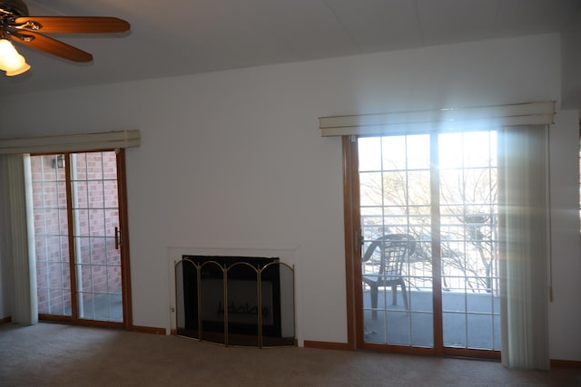 unfurnished living room featuring a fireplace with raised hearth, ceiling fan, and carpet flooring