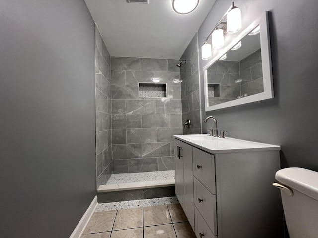 bathroom with toilet, vanity, tile patterned floors, and a tile shower