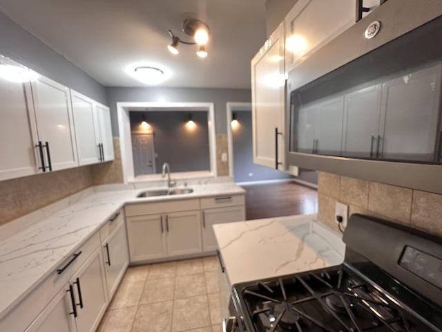 kitchen with sink, white cabinetry, light stone countertops, gas range oven, and light tile patterned floors