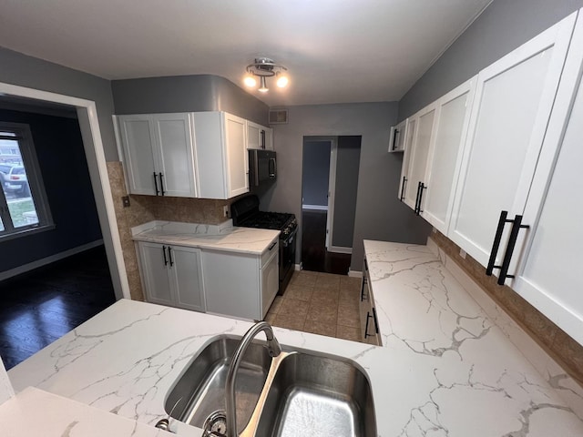 kitchen with light stone counters, sink, white cabinets, and black appliances