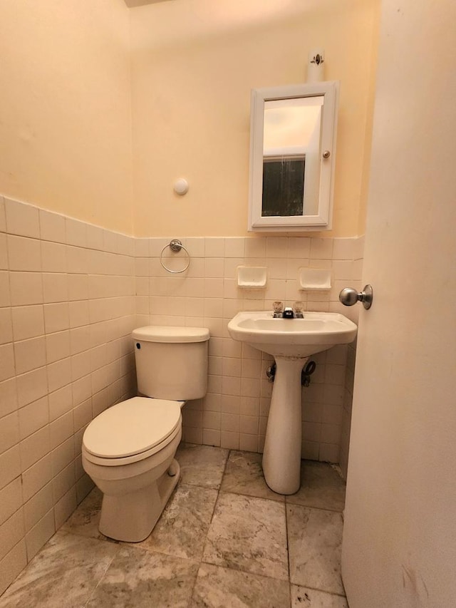 half bath with wainscoting, toilet, tile walls, and a sink