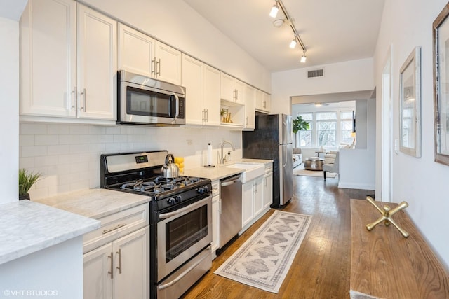 kitchen with dark hardwood / wood-style floors, appliances with stainless steel finishes, white cabinets, and tasteful backsplash