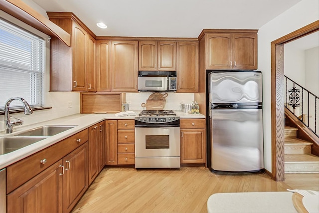 kitchen with sink, light wood-type flooring, appliances with stainless steel finishes, and backsplash