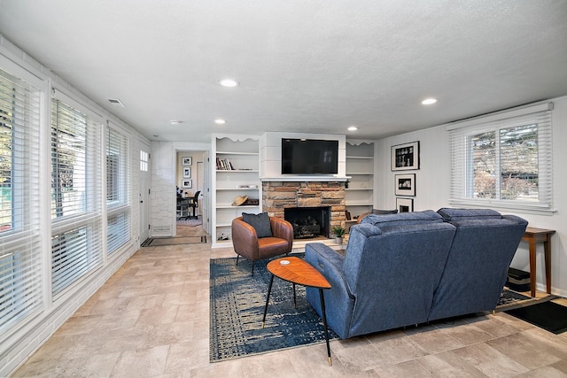 living room featuring a healthy amount of sunlight, a stone fireplace, built in features, and a textured ceiling