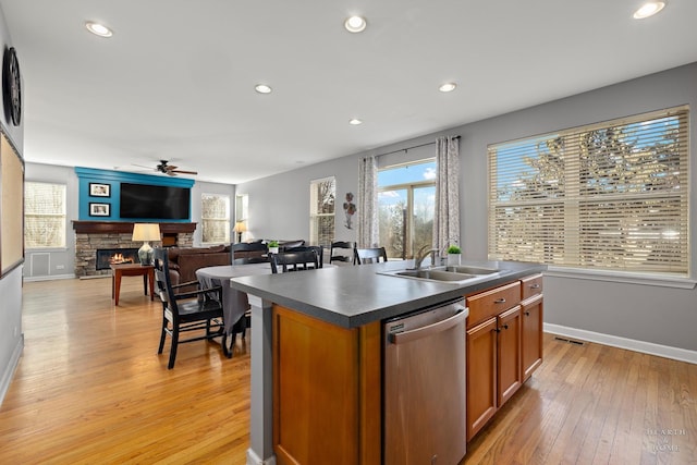 kitchen with dishwasher, sink, light wood-type flooring, a stone fireplace, and a center island with sink