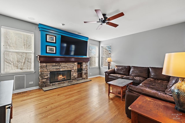 living room with ceiling fan, light hardwood / wood-style flooring, and a stone fireplace