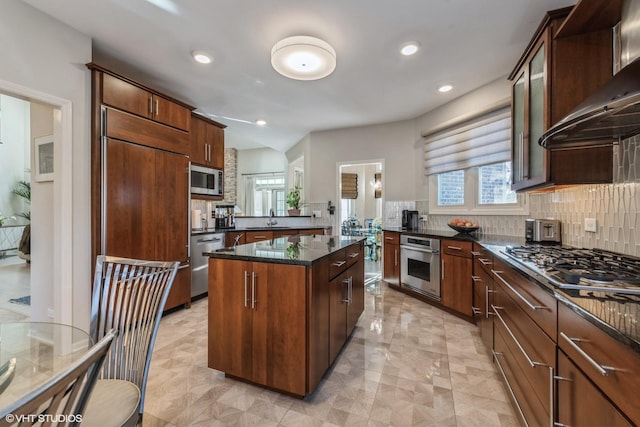 kitchen featuring wall chimney range hood, sink, a center island, built in appliances, and dark stone counters