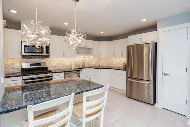 kitchen featuring white cabinets, appliances with stainless steel finishes, decorative light fixtures, a kitchen breakfast bar, and backsplash