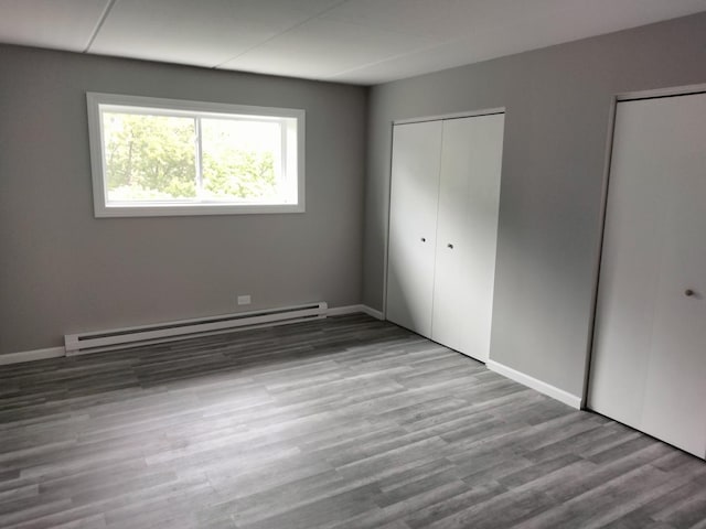 unfurnished bedroom featuring a baseboard heating unit, multiple closets, and light hardwood / wood-style flooring