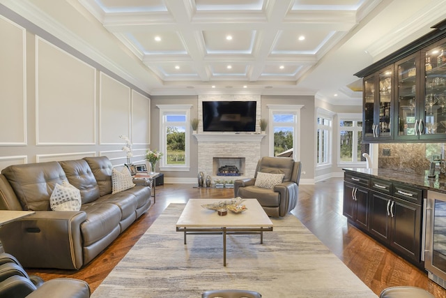 living room with beam ceiling, a healthy amount of sunlight, a stone fireplace, and ornamental molding