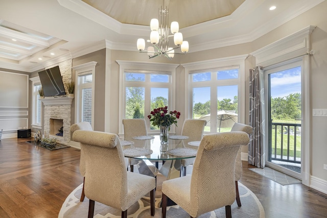 dining space featuring a chandelier, crown molding, a raised ceiling, and a stone fireplace