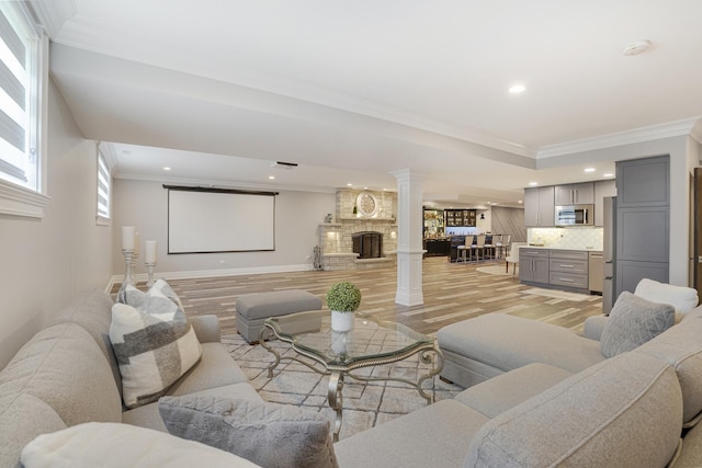 living room with light wood-type flooring, crown molding, plenty of natural light, and decorative columns