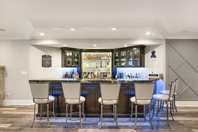 bar with dark wood-type flooring, beamed ceiling, ornamental molding, and dark brown cabinets