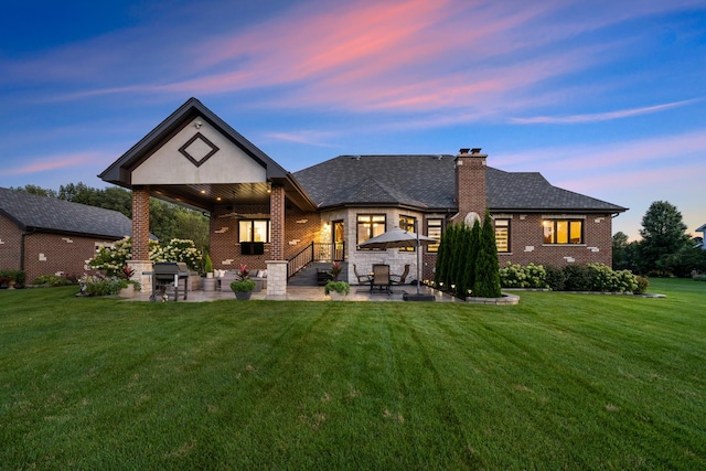 back house at dusk featuring a lawn and a patio