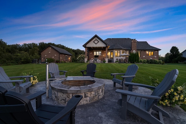 patio terrace at dusk featuring an outdoor fire pit and a lawn