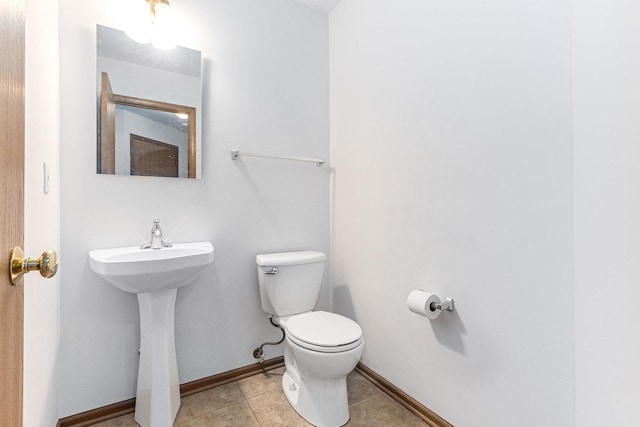 half bath featuring tile patterned floors, toilet, baseboards, and a sink