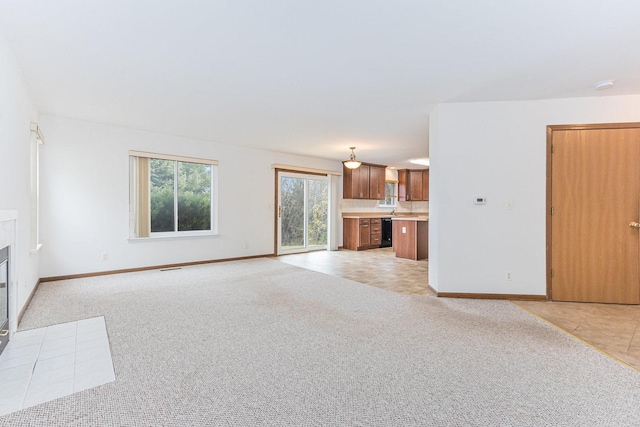 unfurnished living room with a tiled fireplace, light colored carpet, and baseboards