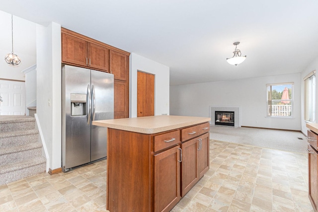 kitchen featuring brown cabinetry, light countertops, stainless steel fridge, a glass covered fireplace, and open floor plan