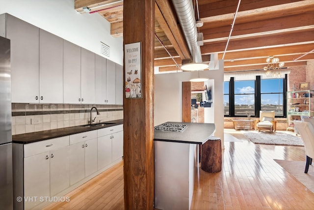 kitchen featuring sink, white cabinetry, beam ceiling, light hardwood / wood-style floors, and backsplash