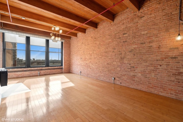 spare room featuring a towering ceiling, brick wall, beam ceiling, and light wood-type flooring