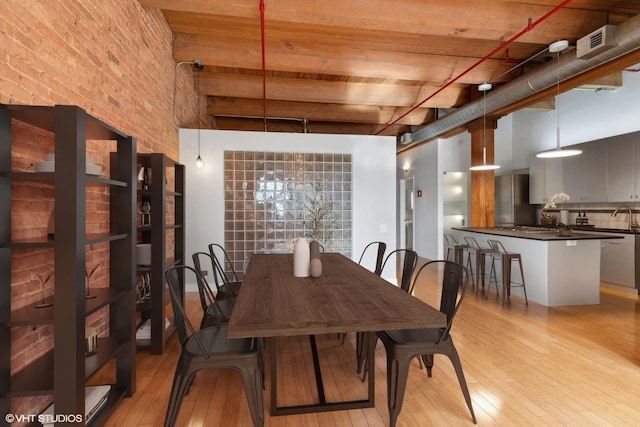 dining space with beamed ceiling, light wood-type flooring, brick wall, a towering ceiling, and sink