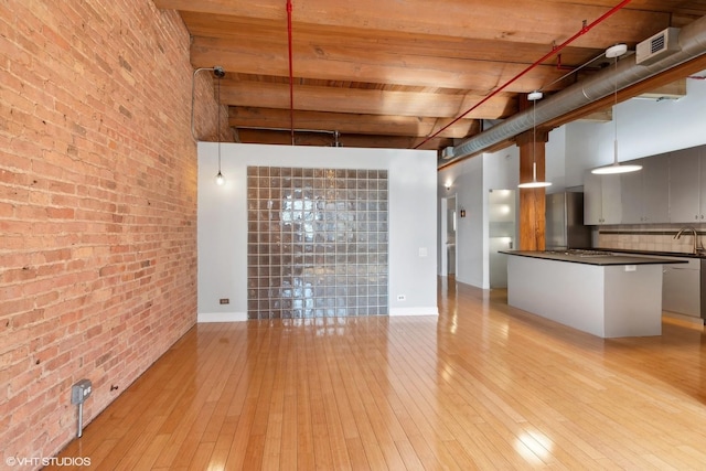 unfurnished living room featuring sink, a towering ceiling, light hardwood / wood-style flooring, and brick wall