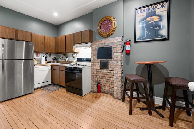 kitchen with gas stove, stainless steel refrigerator, light wood-type flooring, white dishwasher, and a breakfast bar area