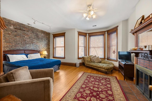 bedroom featuring ceiling fan, hardwood / wood-style floors, a tile fireplace, and track lighting