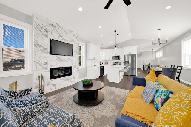 living room with vaulted ceiling, sink, dark hardwood / wood-style flooring, a high end fireplace, and ceiling fan with notable chandelier