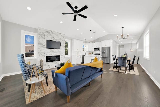 living room with vaulted ceiling, ceiling fan with notable chandelier, dark hardwood / wood-style flooring, and a fireplace