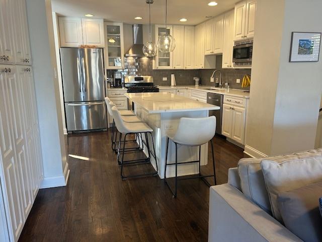 kitchen featuring a kitchen island, pendant lighting, white cabinetry, stainless steel appliances, and wall chimney range hood