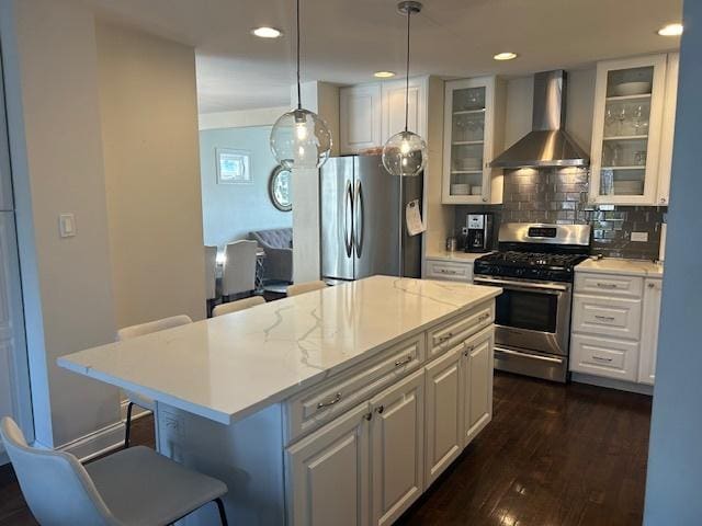 kitchen featuring a kitchen bar, wall chimney range hood, a kitchen island, stainless steel appliances, and white cabinets