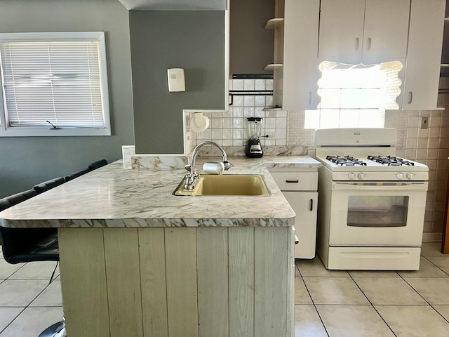 kitchen with white range with gas cooktop, decorative backsplash, sink, kitchen peninsula, and light tile patterned floors